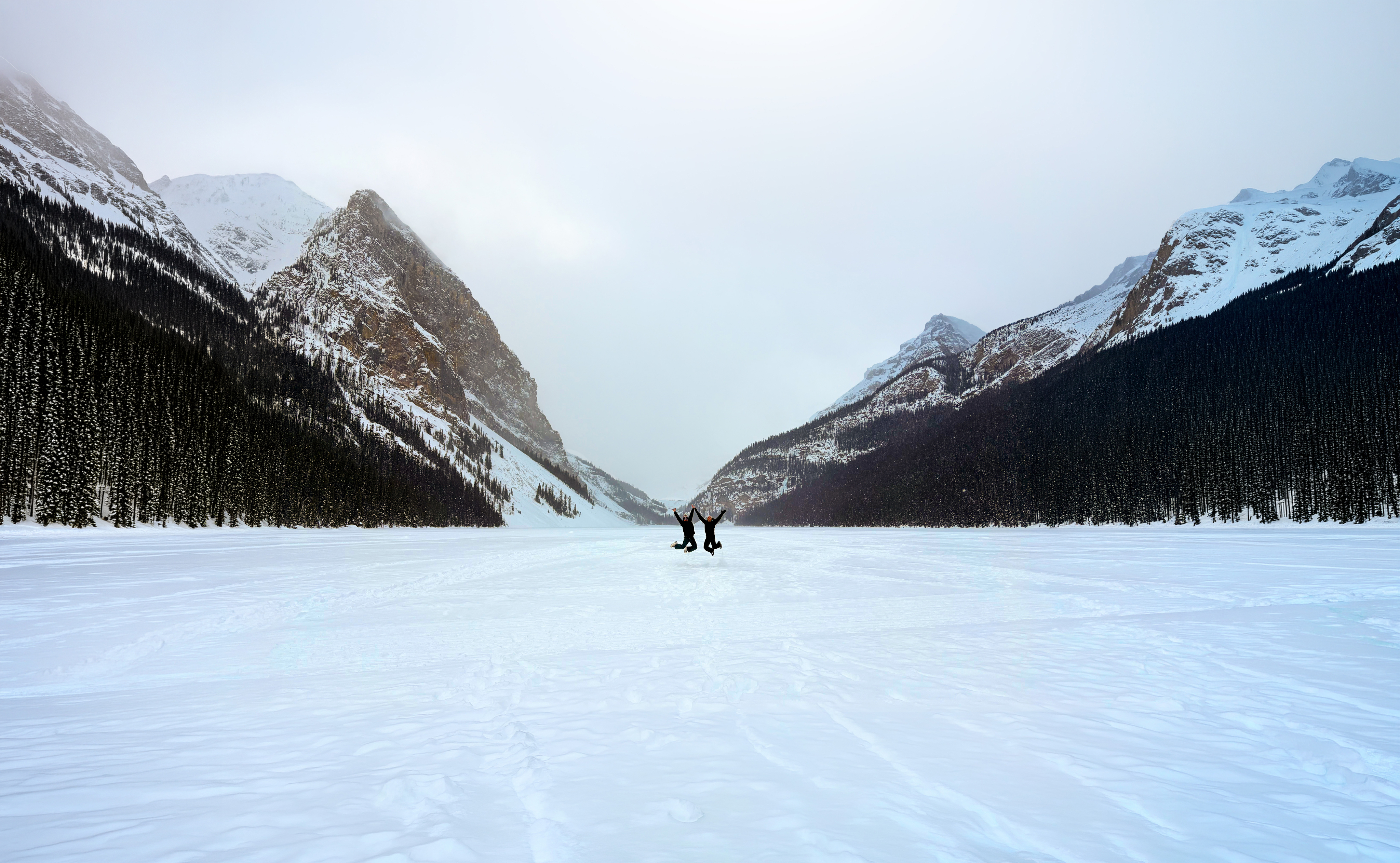 Image of Jason and Lorence at Lake Louise, jumping in unison on the frozen lake with soaring mountains behind them
